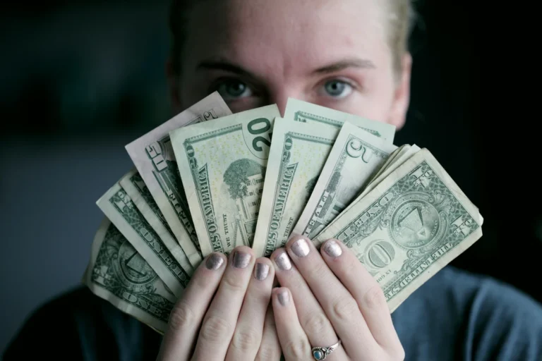 A woman holding a fan of US dollar bills representing passive income ideas and extra cash flow