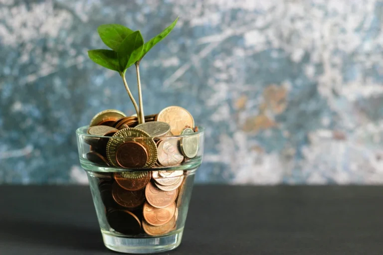 A small green plant growing out of coins in a glass jar representing financial growth and investment