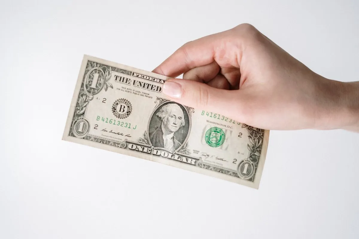 A hand holding a one dollar bill representing regular small investments in dollar cost averaging