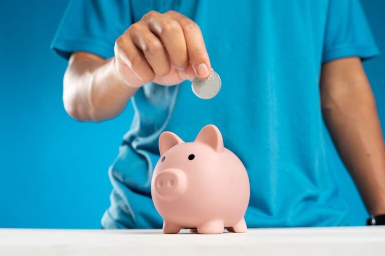 A person putting a coin into a pink piggy bank representing personal savings and money habits