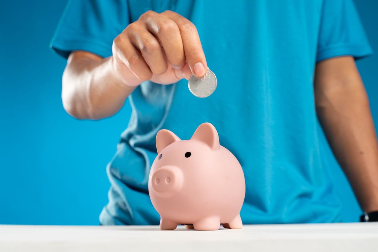 A person putting a coin into a pink piggy bank representing personal savings and money habits
