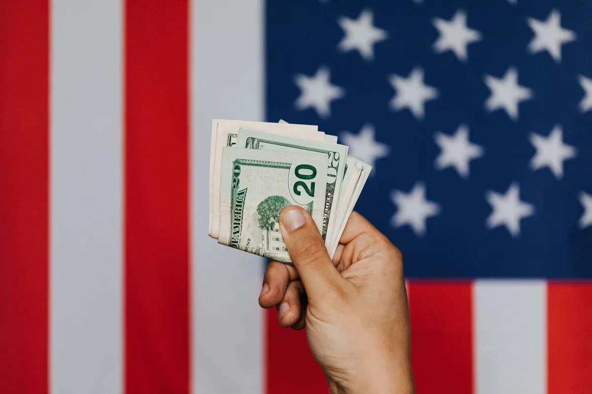 A person holding US dollar bills in front of the American flag representing financial independence