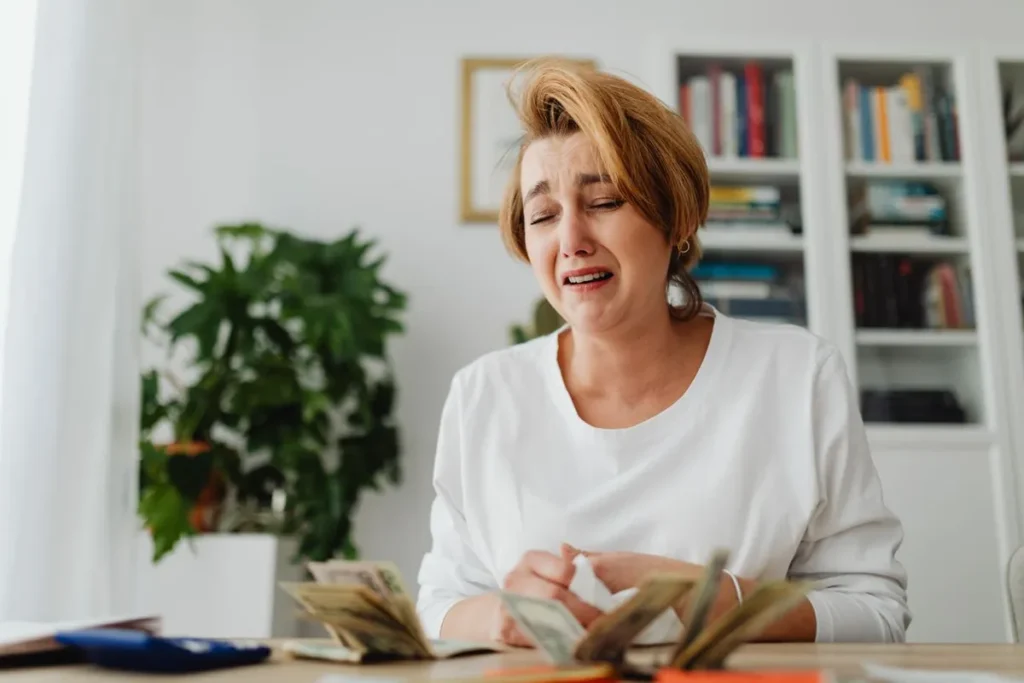 A woman holding her face and looking stressed at her laptop, illustrating Money Mistakes to Avoid.