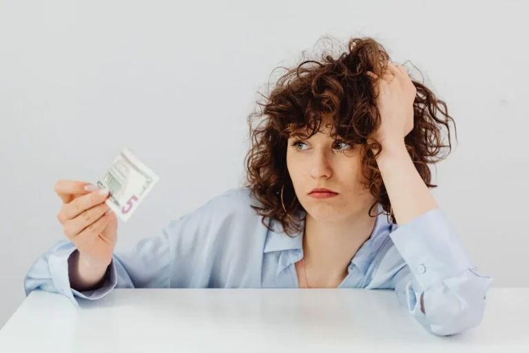 A frustrated woman holding a small amount of money representing financial mistakes and budget struggles