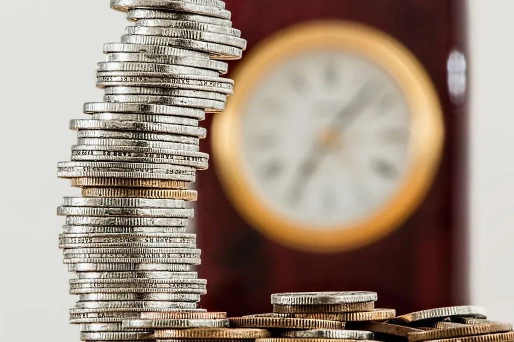 A watch sitting next to a stack of coins, symbolizing the choice between building an Emergency Fund vs Investing.