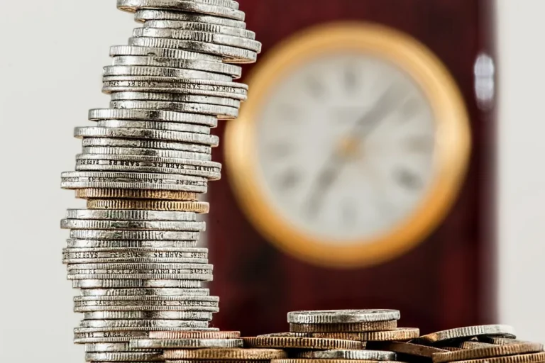 A watch sitting next to a stack of coins, symbolizing the choice between building an Emergency Fund vs Investing.