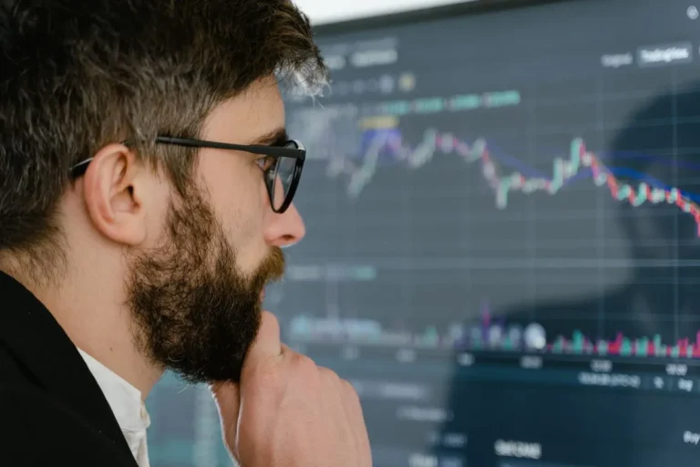 A man with glasses analyzing financial charts on a computer screen representing wealth building and investment strategy