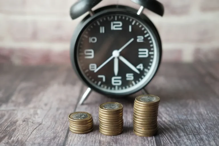 An alarm clock next to growing stacks of coins representing time and compound interest