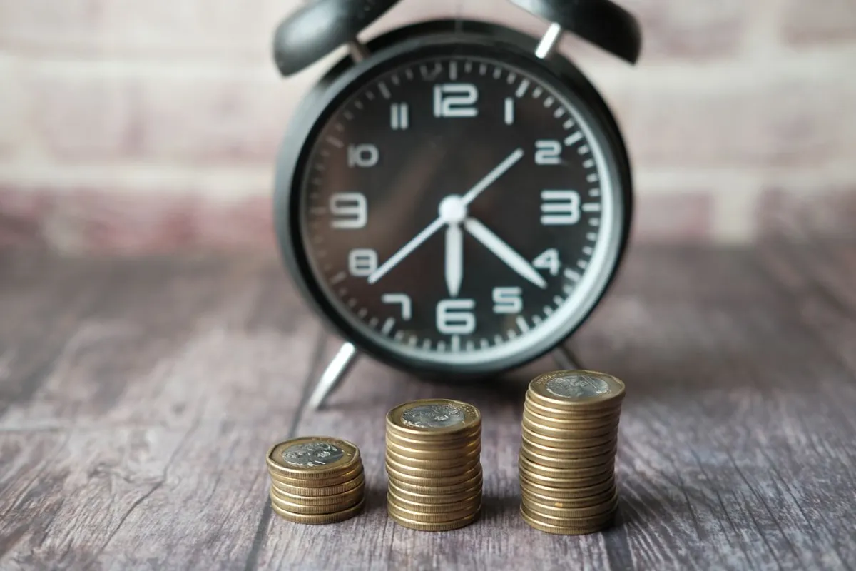 An alarm clock next to growing stacks of coins representing time and compound interest