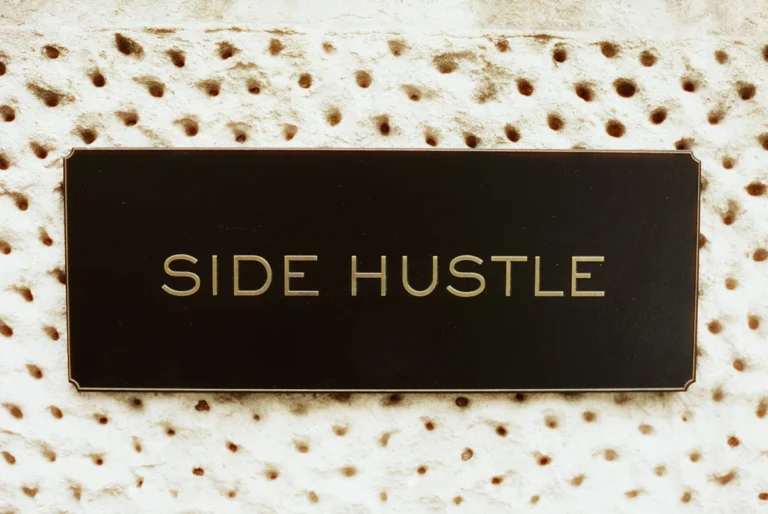 A black plaque displaying the text SIDE HUSTLE in gold letters representing extra income ideas