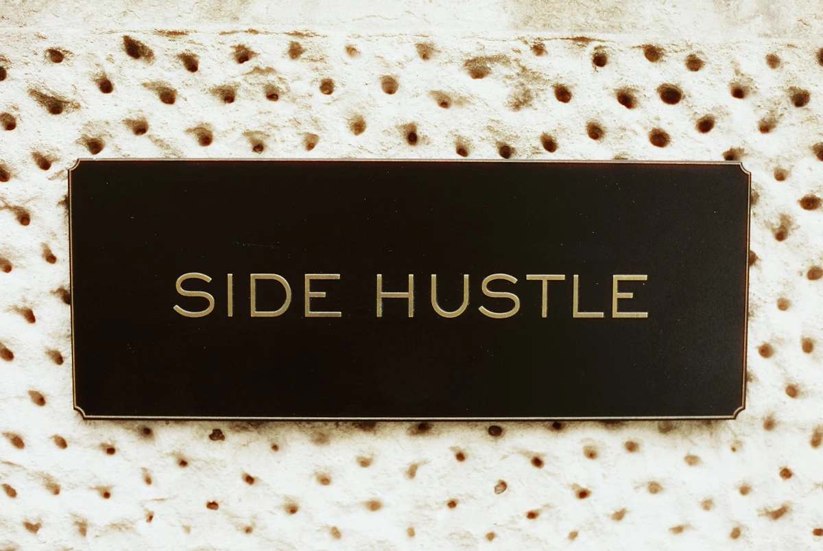 A black plaque displaying the text SIDE HUSTLE in gold letters representing extra income ideas