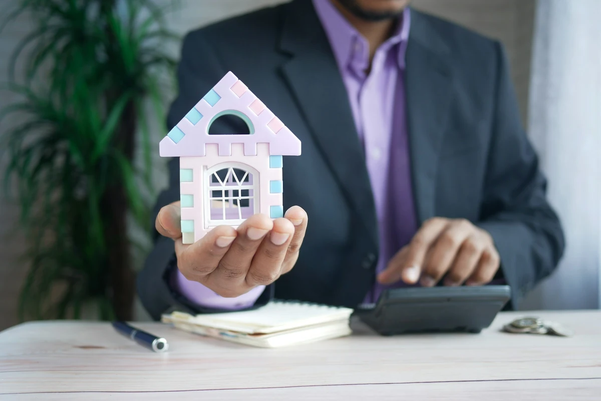 A person holding a small house and keys, symbolizing home insurance coverage