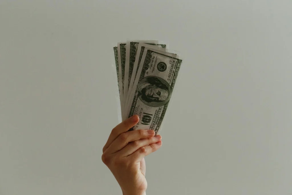 A hand holding a stack of US dollar bills representing How to Improve Your Finances