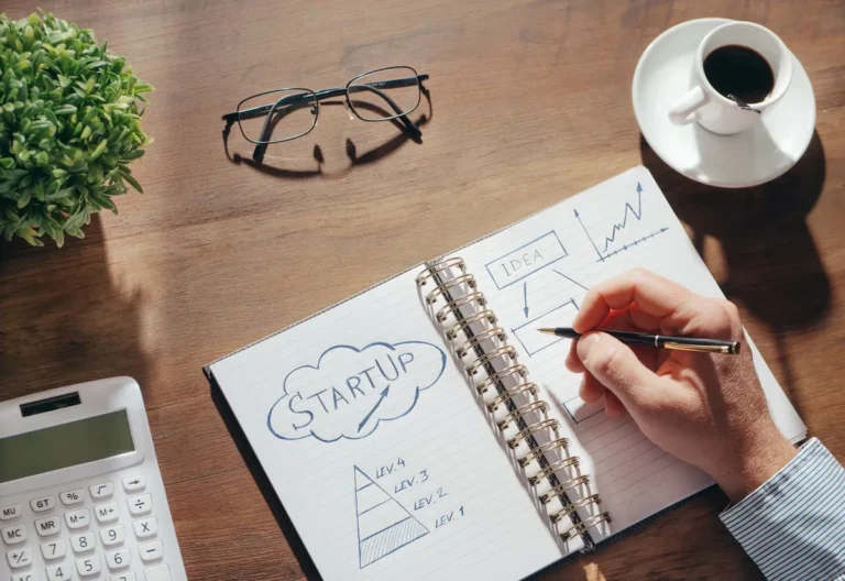 An image representing the guide on "How Startups Raise Money," showing hands working over financial documents, glasses, and a smartphone.