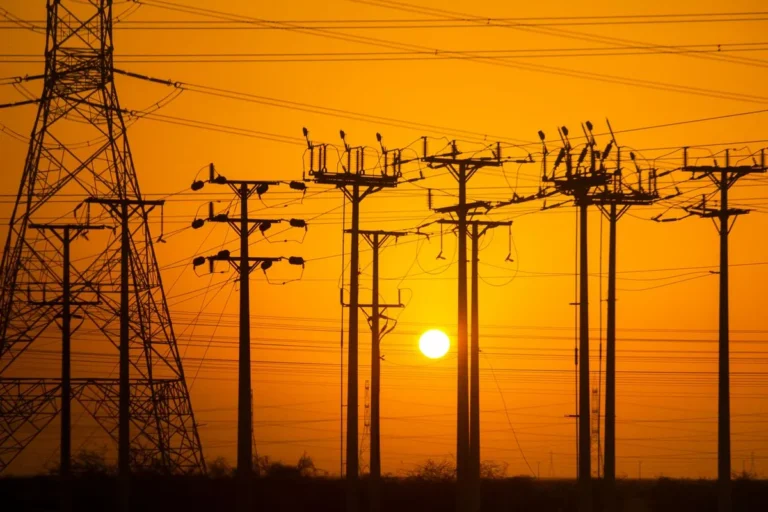 Silhouette of power transmission towers and electric lines against a dramatic warm sunset sky, illustrating Energy Markets in Transition.