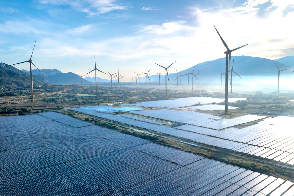 Wind turbines and solar panels on a green field under a clear blue sky, illustrating renewable energy investment opportunities in clean tech and power infrastructure