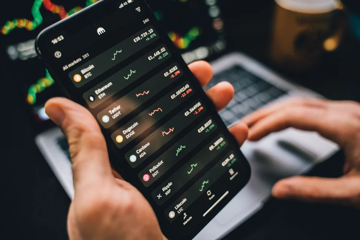 What Is a Crypto Wallet? - Person holding a smartphone displaying crypto trading apps and digital asset charts.