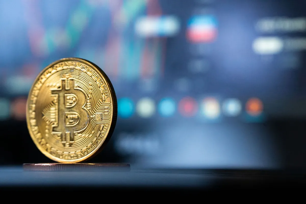 A glowing digital physical cryptocurrency coin resting on a smartphone screen showing financial charts, illustrating What is Decentralized Finance (DeFi) and digital asset markets.