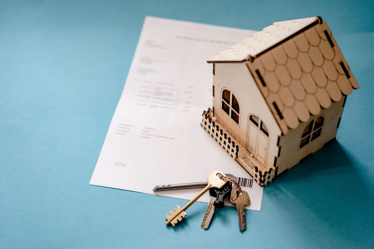 A miniature model house placed on architectural blue plans with keys and a pen, representing how mortgage loans work for home financing.