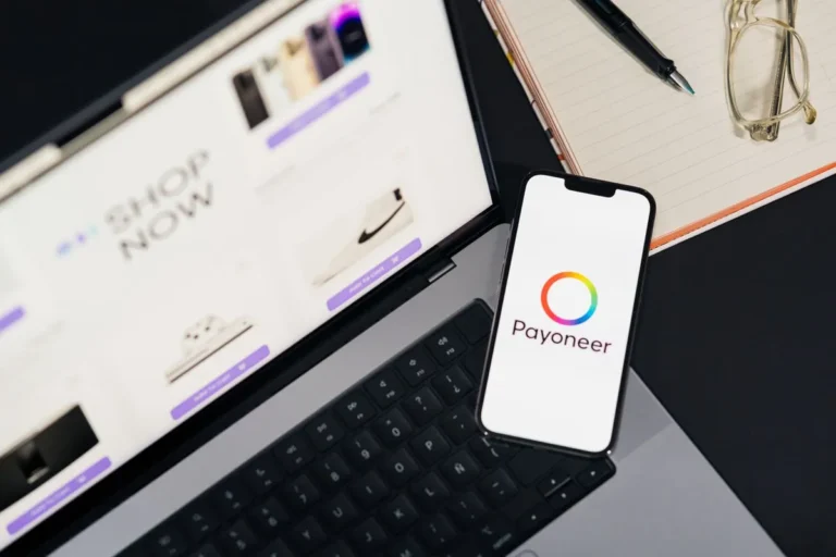 Smartphone displaying the Payoneer platform alongside a laptop and financial documents on a desk — What Is Payoneer?