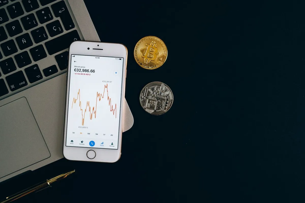 Smartphone showing cryptocurrency trading charts next to physical Bitcoin and digital asset coins, representing the top 10 cryptocurrency exchanges in 2026.