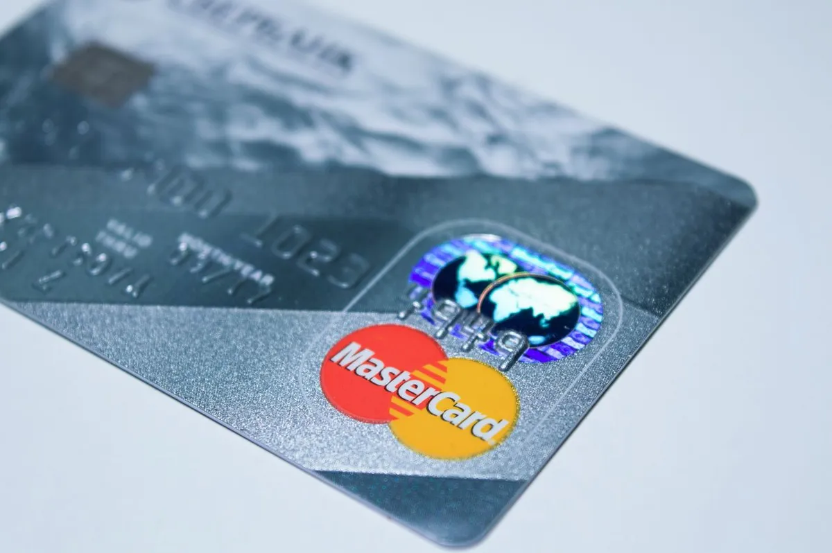 Credit card with a Mastercard logo held over a payment terminal, illustrating what is Mastercard and how payment processing networks work.